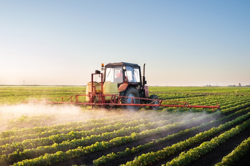 Ein Traktor versprüht auf einem grünen Feld eine Flüssigkeit.