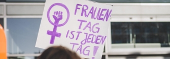 Personen auf einer Demo mit Protestschild. Text: Frauentag ist jeden Tag!