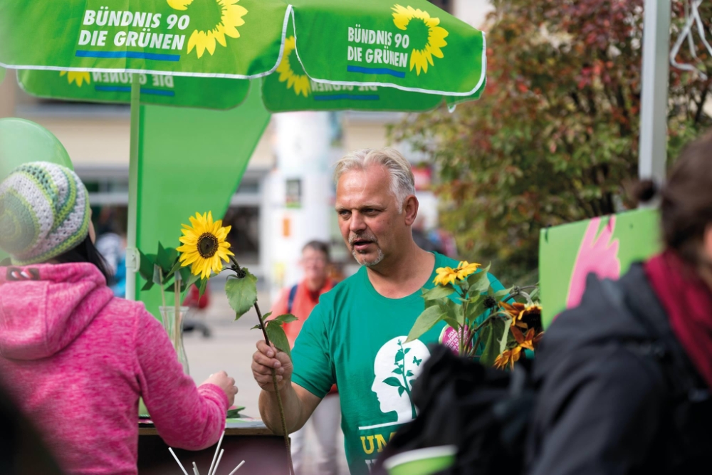 Grünes Mitglied verteilt Sonnenblumen an Passant*innen.