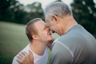 Vater und Sohn lächeln sich an und halten die Stirn nah aneinander.