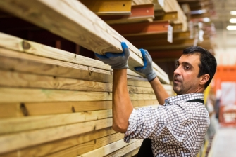 Ein Mann hebt Holzbretter von einem Stapel.