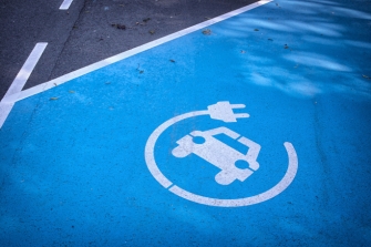Parkplatz mit bemaltem Boden in Blau mit Icon. Icon: Auto mit Kreis in der Optik eines Elektrokabels