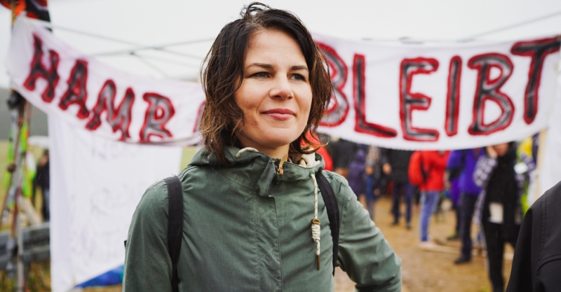 Porträt von Annalena Baerbock vor einem Protestbanner mit dem Text "Hambi bleibt".